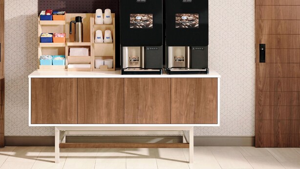A modern kitchen with wooden cabinets, a white countertop, and two coffee machines. - Holiday Inn Express Atlanta Airport - College Park by IHG (College Park)
