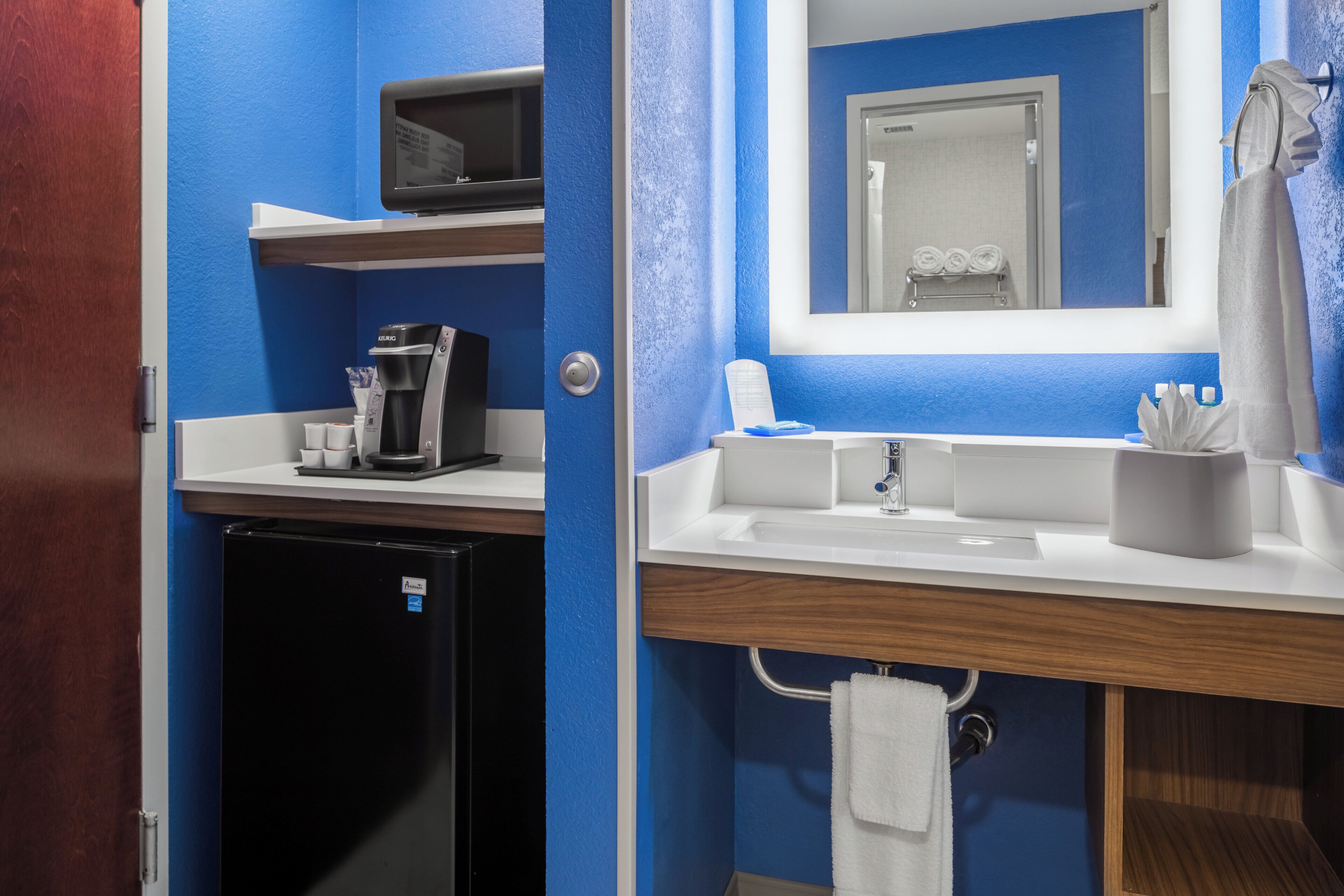 A compact hotel bathroom with a coffee maker, a sink, and a mirror.