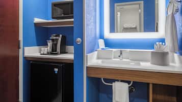 A compact hotel bathroom with a coffee maker, a sink, and a mirror.