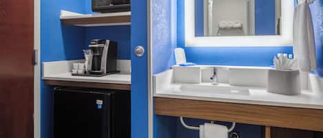 A compact hotel bathroom with a coffee maker, a sink, and a mirror.