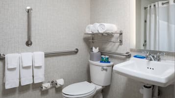 A bathroom with a toilet, handrails, a sink, and a towel rack.