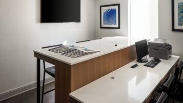A modern office space with a long desk, a flat-screen monitor, a printer, and framed artwork on the walls.