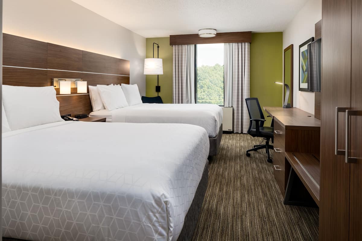 A hotel room with two beds, a desk, a chair, a TV, and a window with curtains.