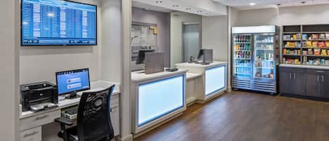 A modern airport check-in area with digital displays, a Holiday Inn Express sign, and a vending machine.