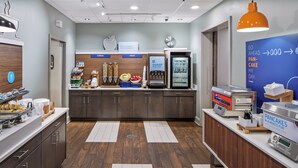 A breakfast area with a coffee machine, fruit display, and a sign for a Pan-Cake Express. - Holiday Inn Express Atlanta Airport - College Park by IHG (College Park)