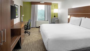 Habitación de hotel con cama, escritorio, silla, televisión y ventana con cortinas.