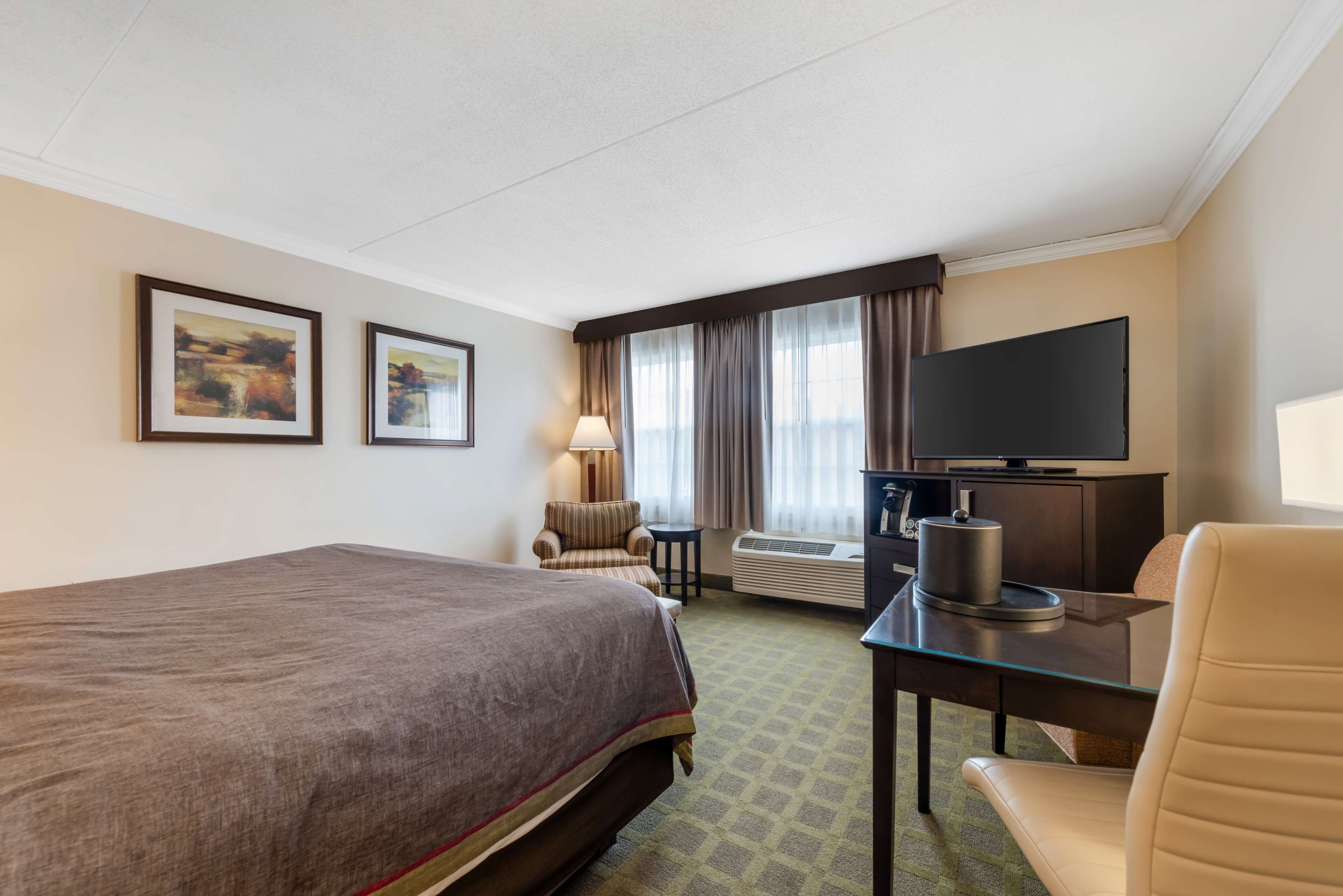 Une chambre d’hôtel avec un grand lit, un bureau doté d’un téléviseur à écran plat, une chaise, une lampe et deux tableaux encadrés au mur.