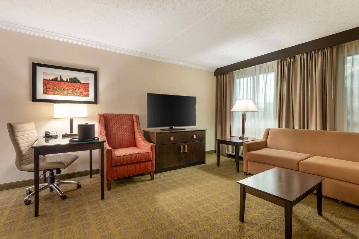 A hotel room with a desk, chair, sofa, TV, and a framed picture on the wall.