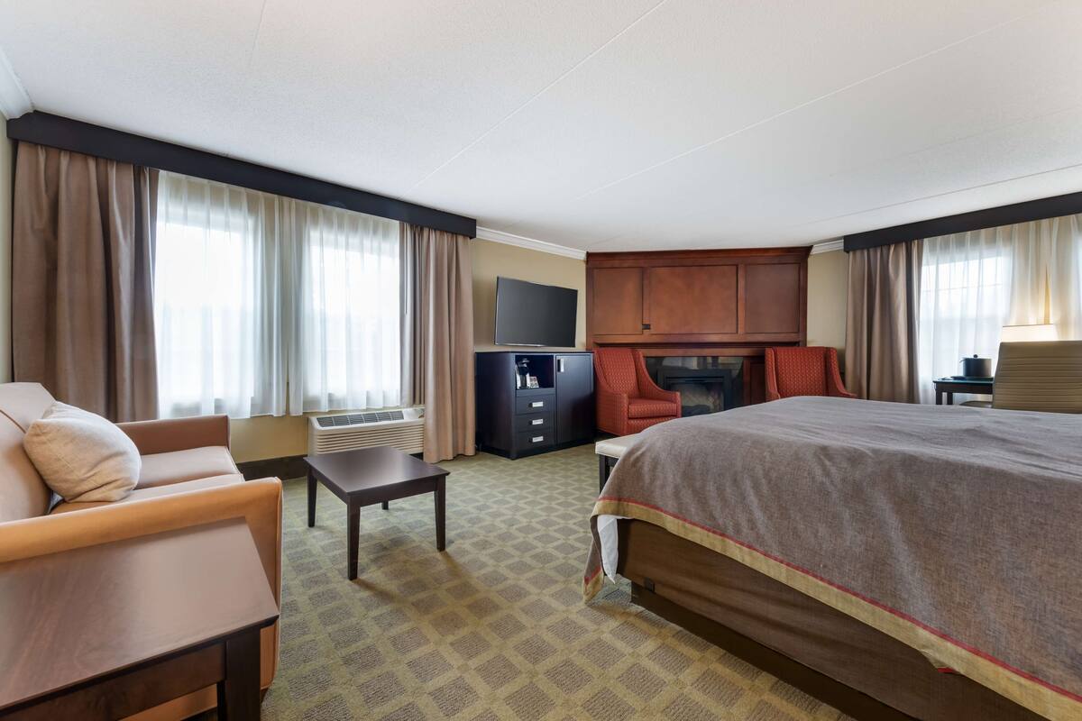 A hotel room with a large bed, a sofa, a desk, a TV, and a cabinet.