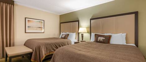 A hotel room with two beds, a bench, a painting, and a lamp.