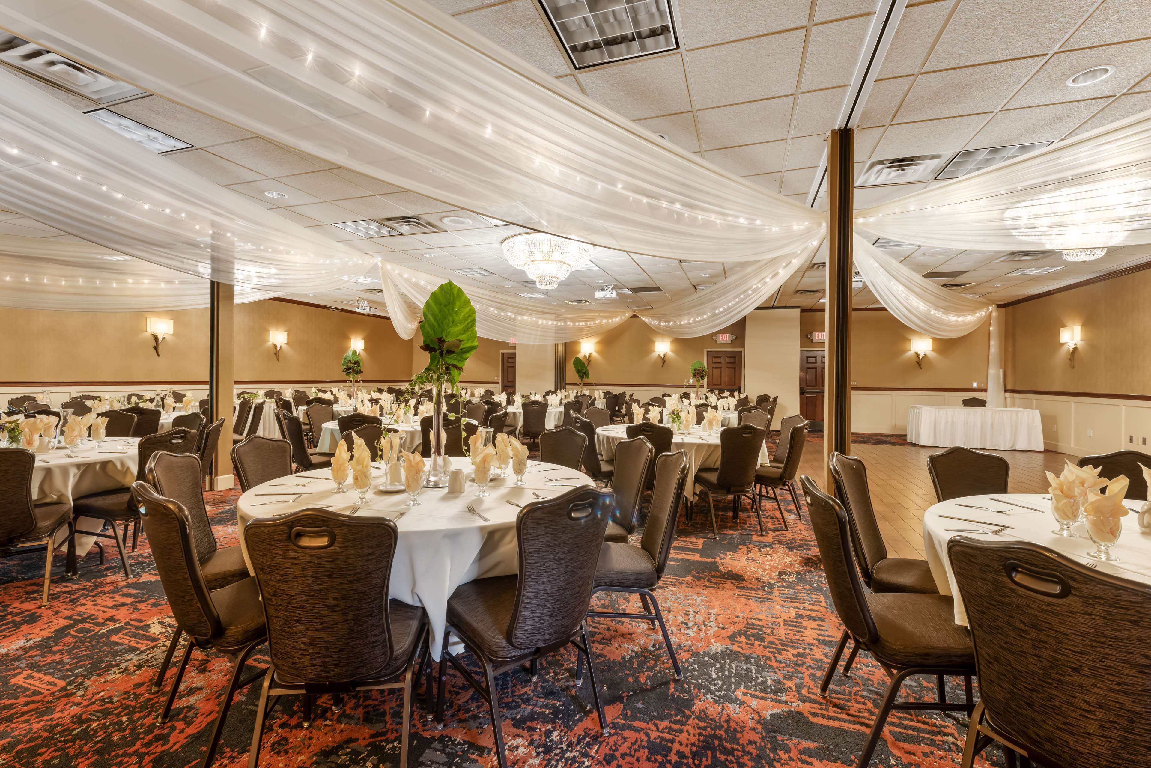 Un salón de banquetes con mesas redondas, sillas y tela decorativa en el techo.