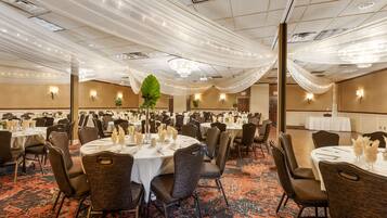 Un salón de banquetes con mesas redondas, sillas y tela decorativa en el techo.