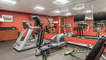 A gym with cardio machines, weight benches, and a mirrored wall.