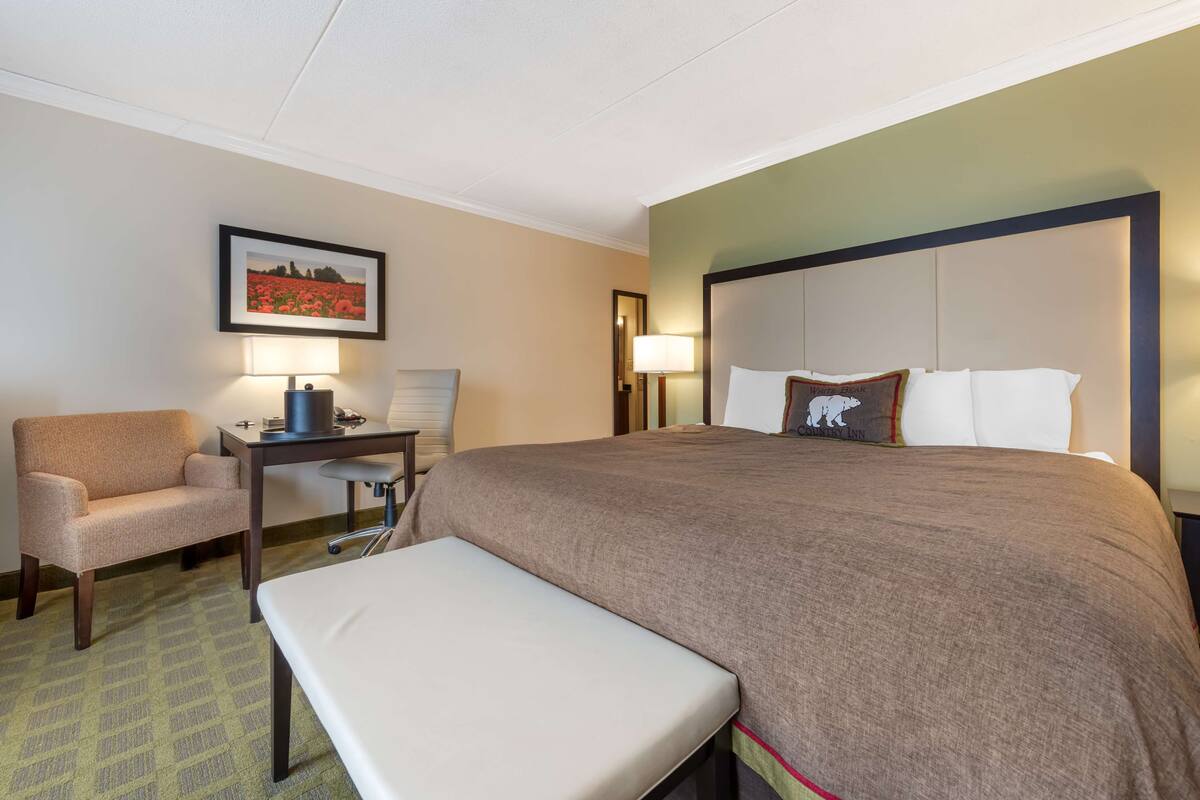 A hotel room with a large bed, a desk, a chair, and a bench.