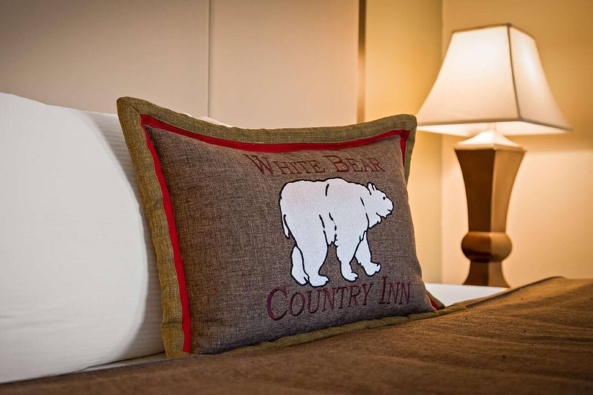A bed with a white pillow and a decorative pillow with a bear design and text.