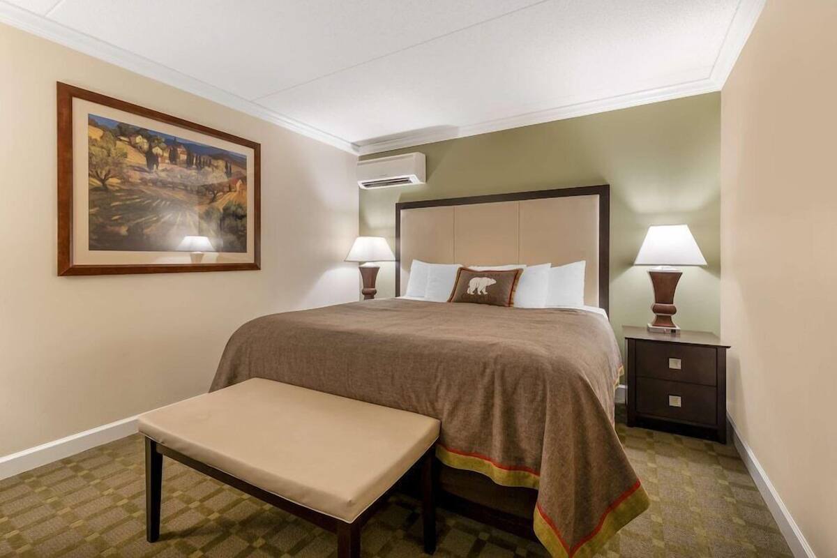 A hotel room with a bed, two bedside tables with lamps, a bench, and a framed painting on the wall.