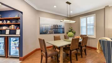 Un comedor con mesa de madera, seis sillas, una planta en maceta y un cuadro de un paisaje urbano en la pared.
