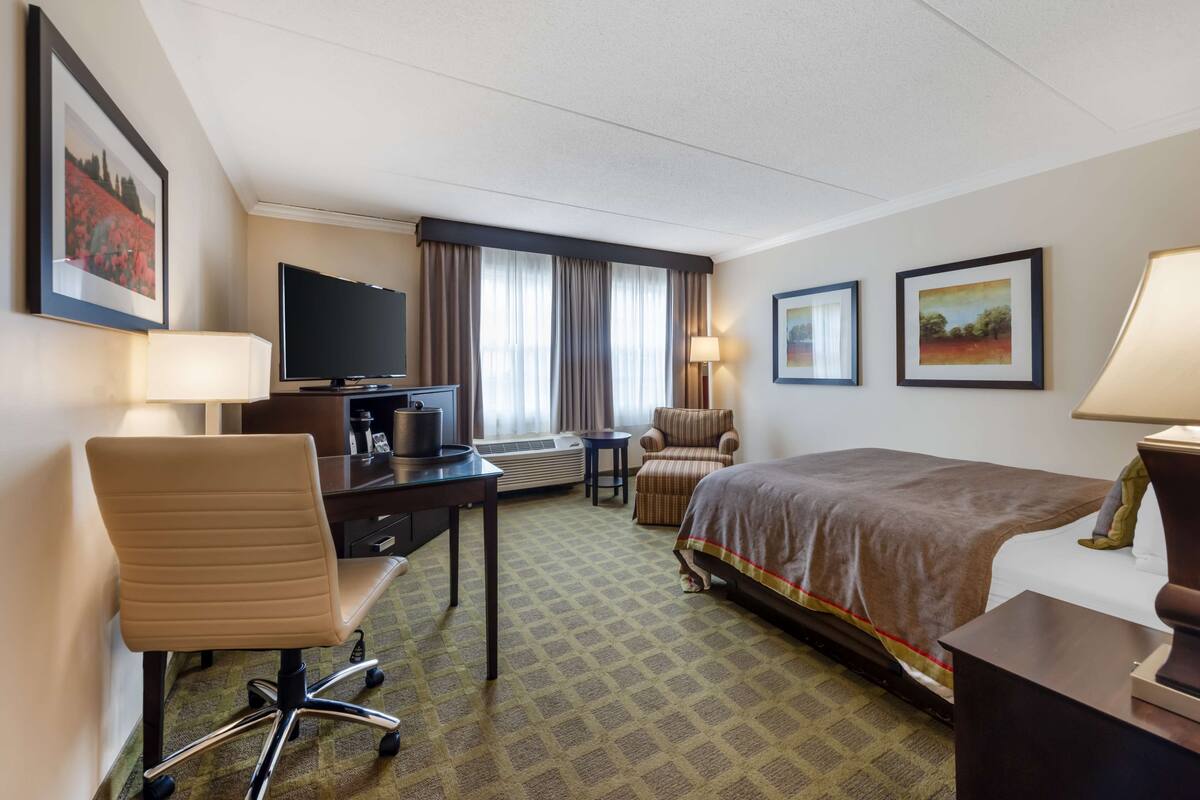 A hotel room with a bed, a desk with a television, a chair, and a window with curtains.