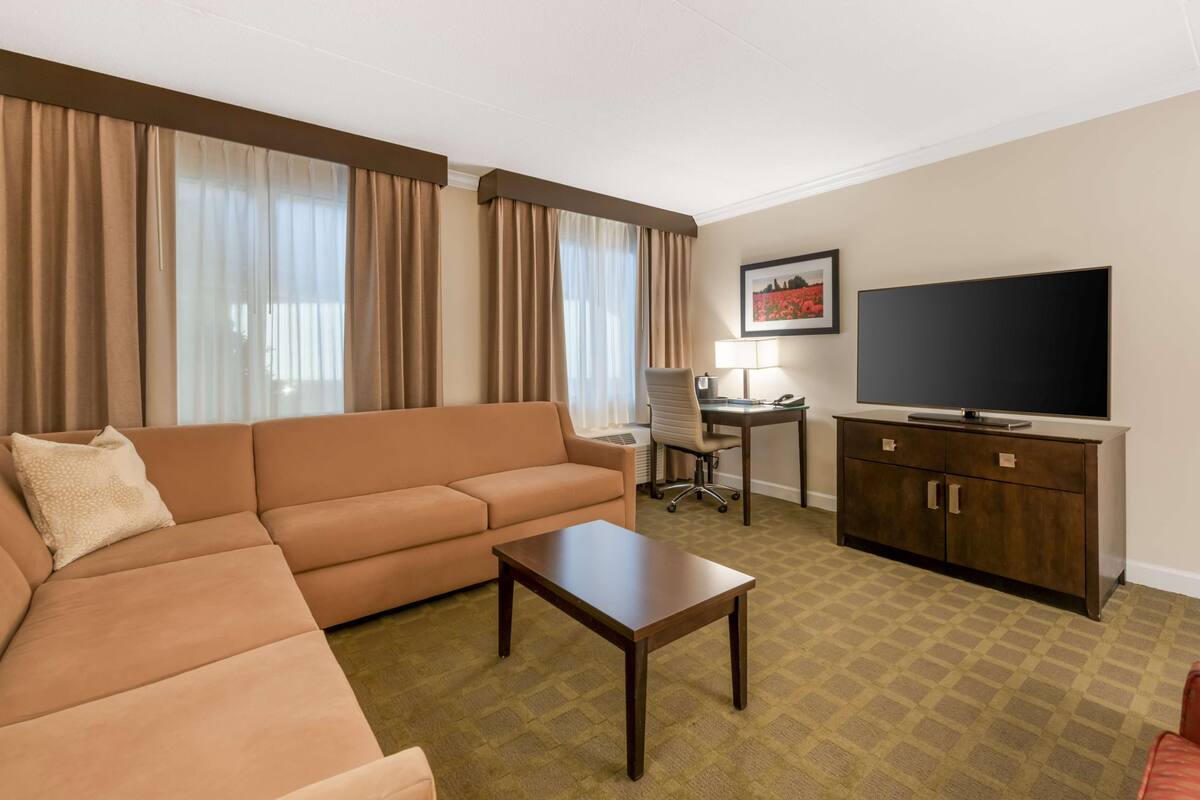 A hotel room with a sofa, a coffee table, a desk with a chair, a television, and a cabinet.
