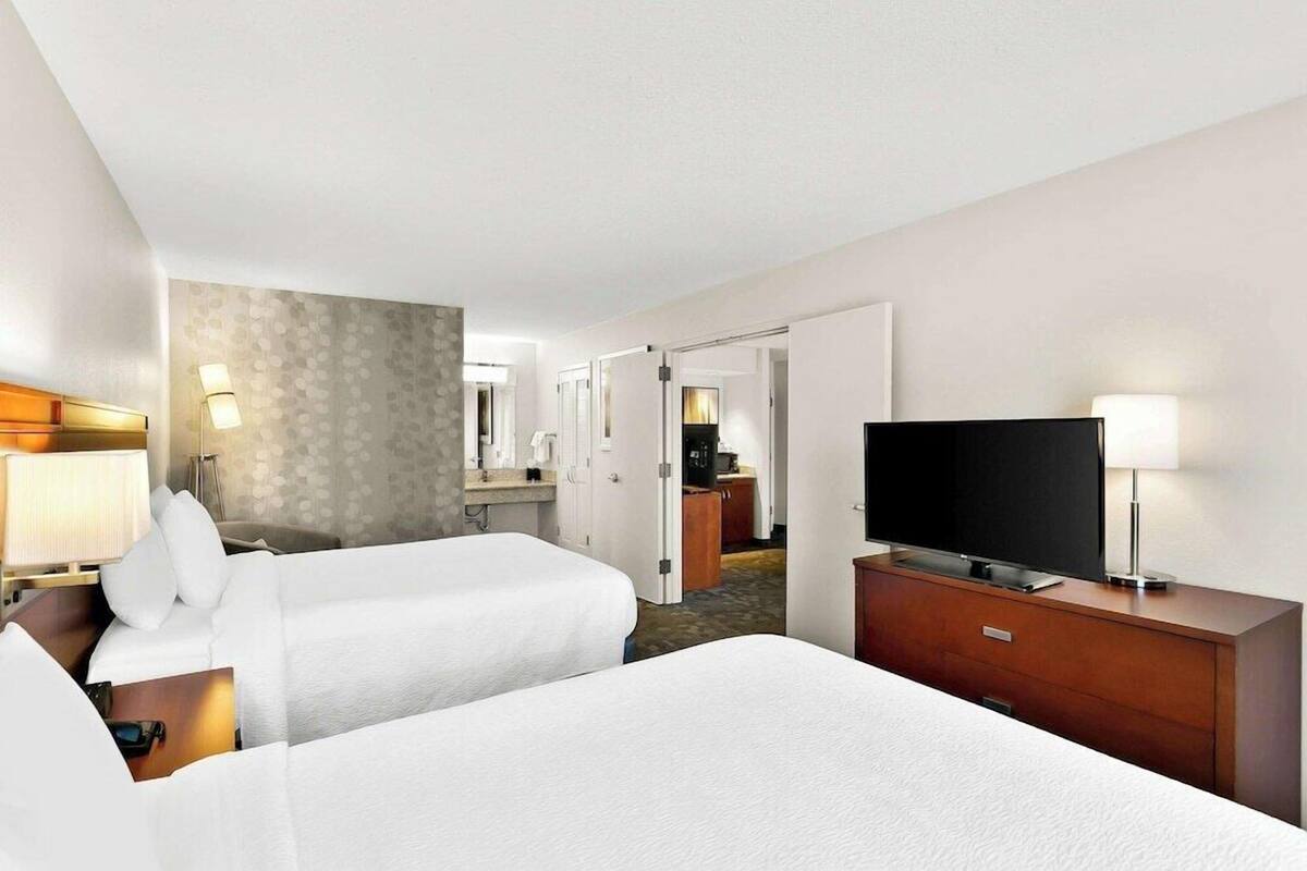 Ein Hotelzimmer mit zwei Betten, einem Fernseher, einem Schminktisch und einem durch eine offene Tür einsehbaren Badezimmer.