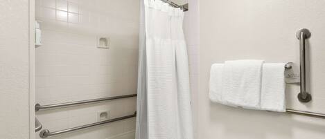 A bathroom with a shower, grab bars, a towel rack, and a toilet paper holder.