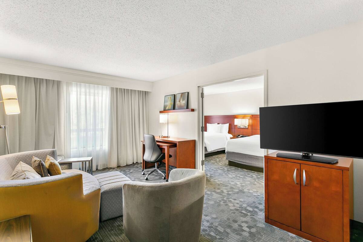 Ein Hotelzimmer mit einer Couch, einem Schreibtisch, einem Fernseher und einem Bett.