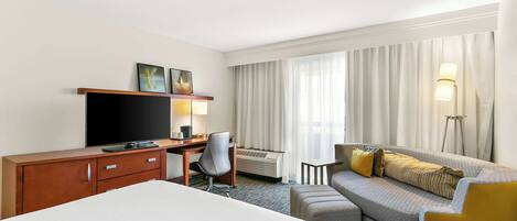 Una habitación de hotel con una cama, un escritorio con televisor, un sofá y una silla.
