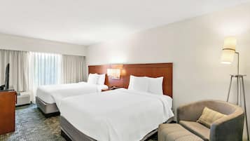 A hotel room with two beds, a desk, a chair, and a floor lamp.