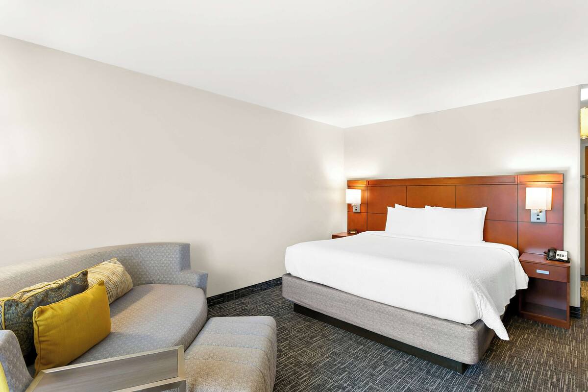 Ein Hotelzimmer mit Bett, Sofa, Nachttisch und einer Wandlampe.