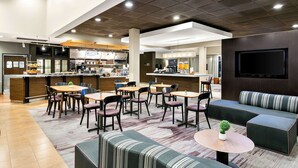 Een moderne hotel lobby met een bar, zithoekjes en een televisiescherm.