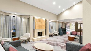 Een moderne hotellobby met een open haard, zitgedeeltes en een grote poster.
