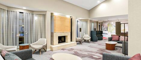 A modern hotel lobby with a fireplace, seating areas, and a large poster.