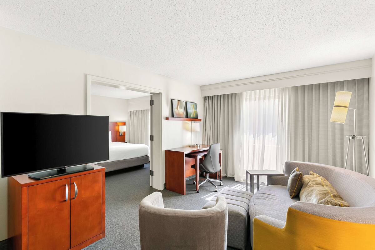 Ein Hotelzimmer mit Fernseher, Schreibtisch, Stuhl, Sofa und Bett.
