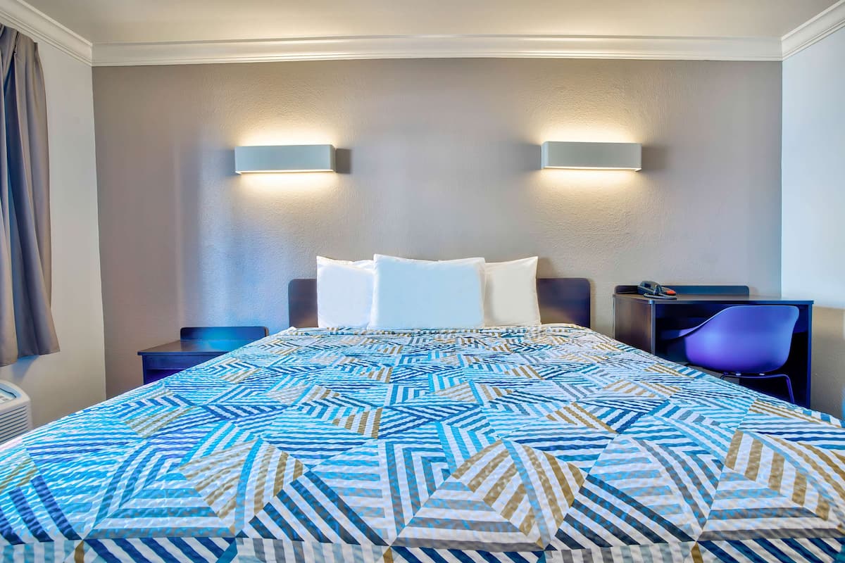 Quarto de hotel com uma cama grande, duas mesas de cabeceira, uma escrivaninha com cadeira e duas luminárias de parede.