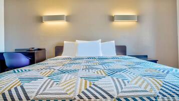 Habitación de hotel con una cama bien hecha, dos mesitas de noche, una silla y lámparas de pared.
