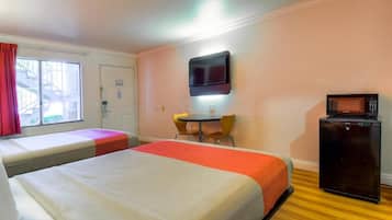 A hotel room with two beds, a TV mounted on the wall, a small table with chairs, and a refrigerator.