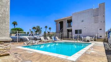 A swimming pool with lounge chairs and a building with a balcony.