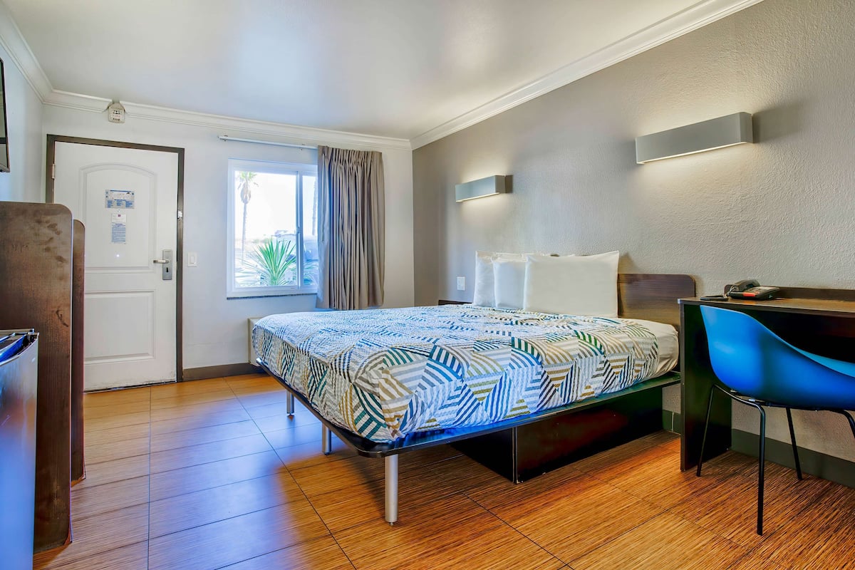 Quarto de hotel com cama, secretária, cadeira, janela com cortinas e porta.