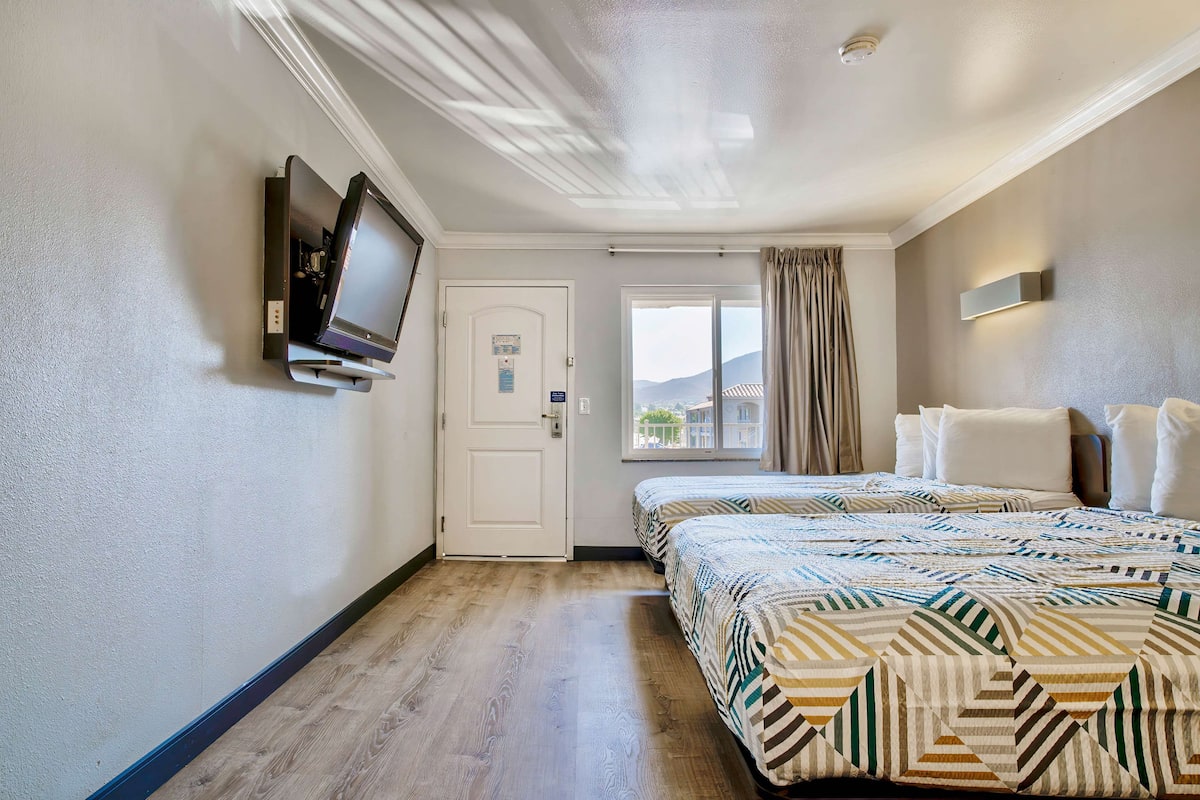 Quarto de hotel com cama, televisão na parede, porta e janela com cortinas.