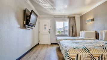 Hotellihuone, jossa on sänky, seinälle asennettu televisio, ovi ja ikkuna, jossa on verhot.
