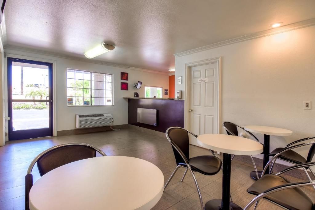 A hotel room with a reception desk, a television, a door, and a seating area with tables and chairs.