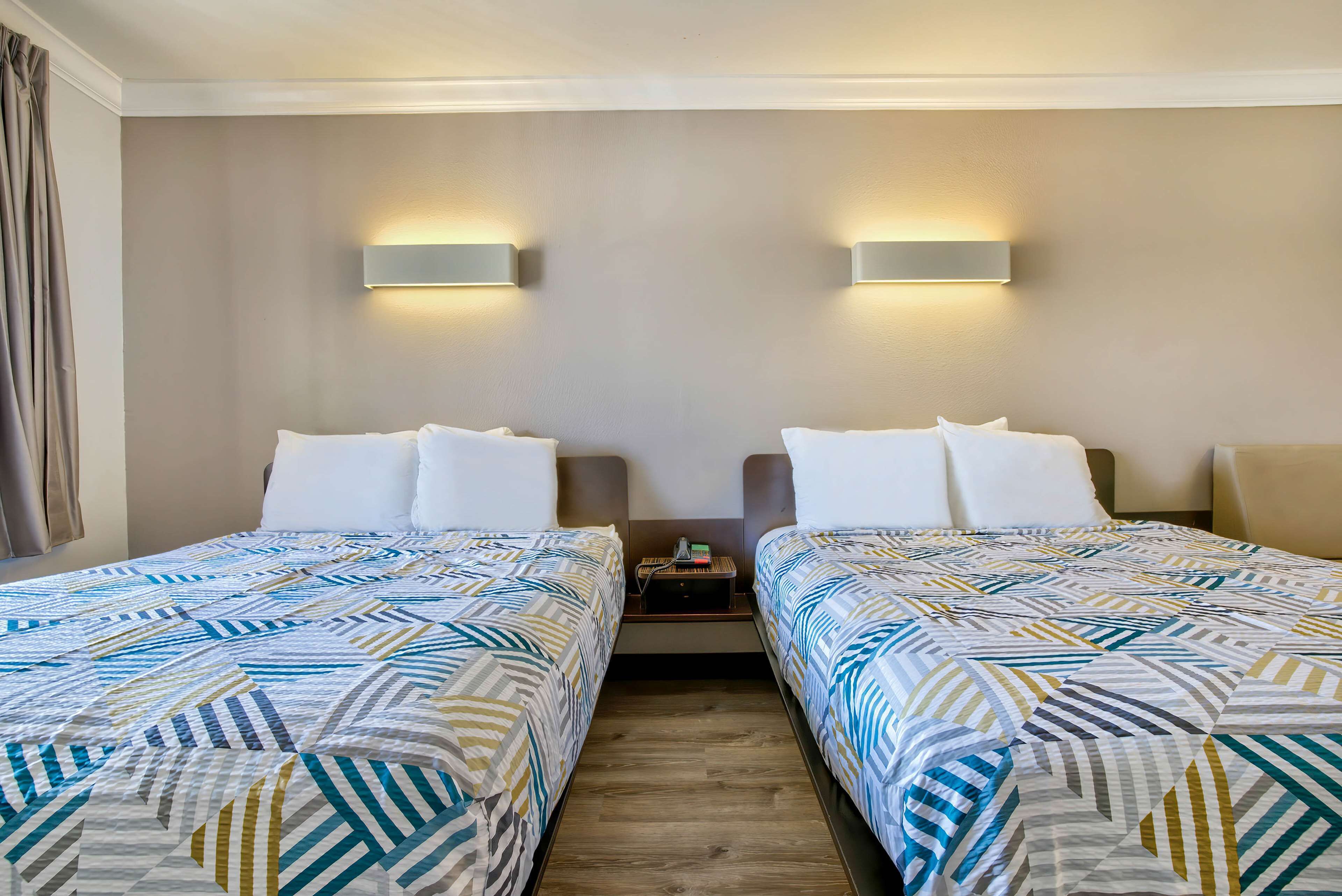 Une chambre d’hôtel avec deux lits, chacun recouvert d’une couvre-lit à motifs, une table de chevet entre les deux, et des lampes fixées au mur.