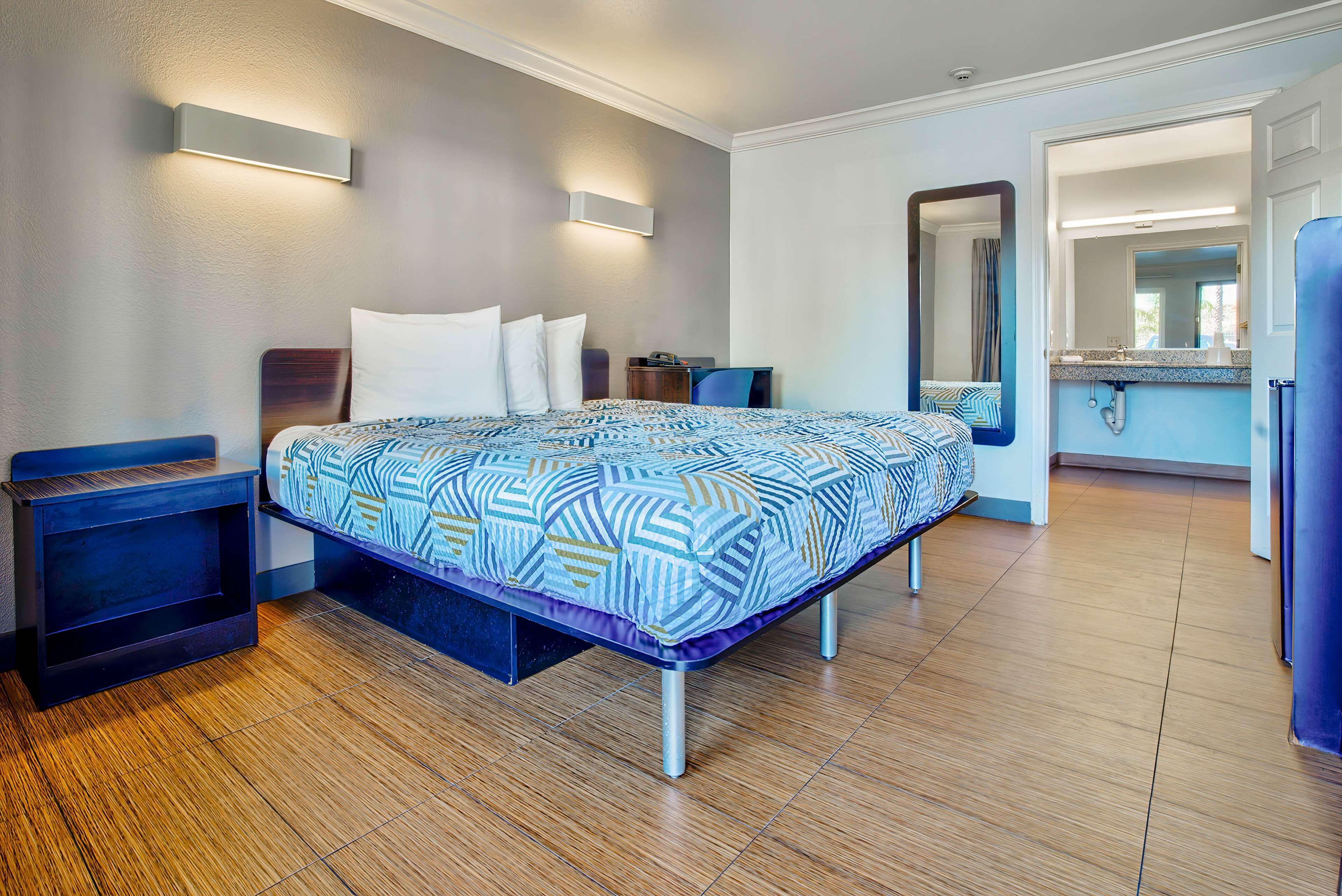 Habitación de hotel moderna con una cama bien hecha, una mesita de noche, un pequeño escritorio y un baño visible a través de una puerta abierta.