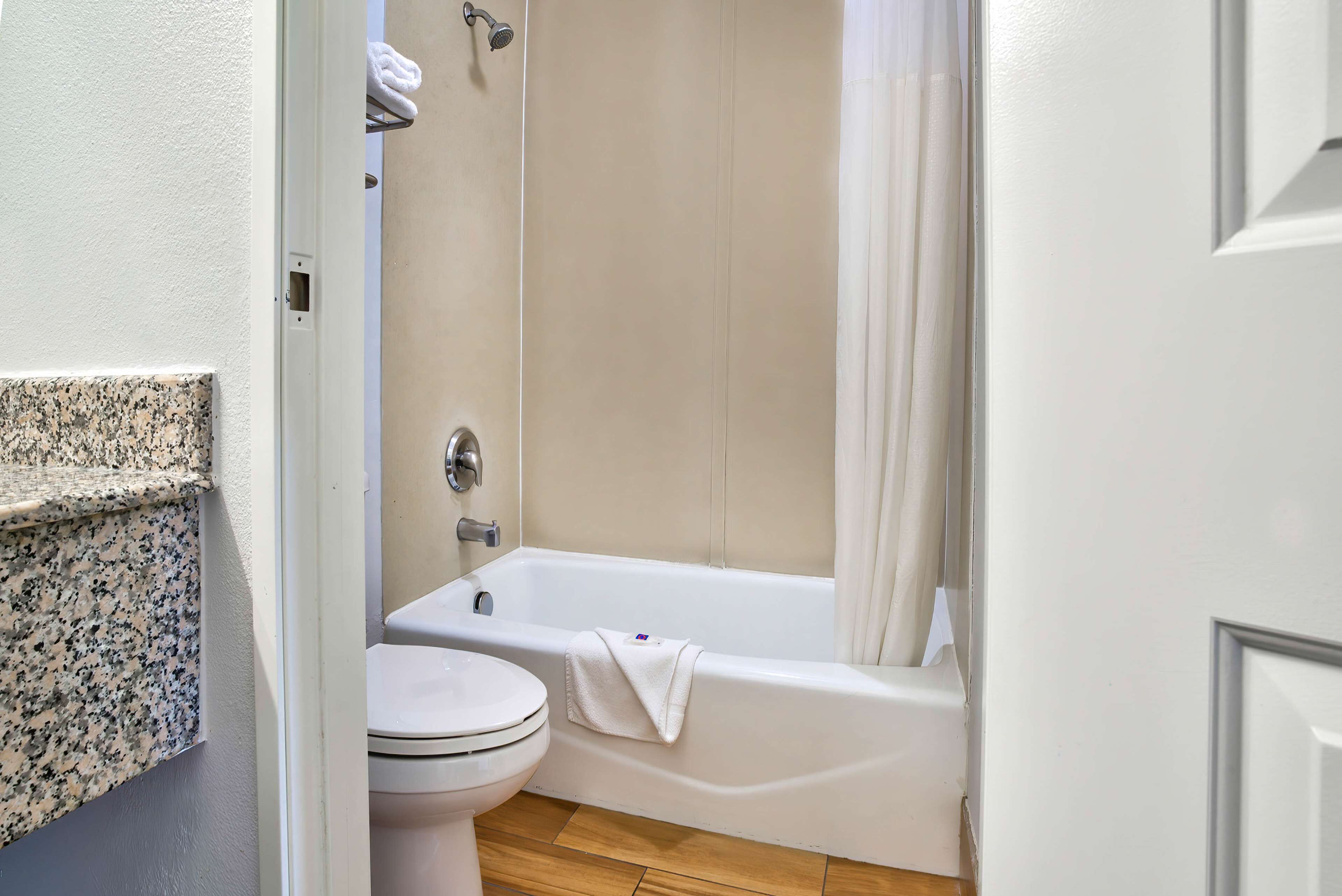 Un baño con inodoro blanco, bañera con toalla y cortina de ducha.