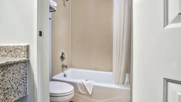 A bathroom with a white toilet, a bathtub with a towel, and a shower curtain.