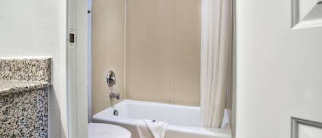 Un baño con inodoro blanco, bañera con toalla y cortina de ducha.
