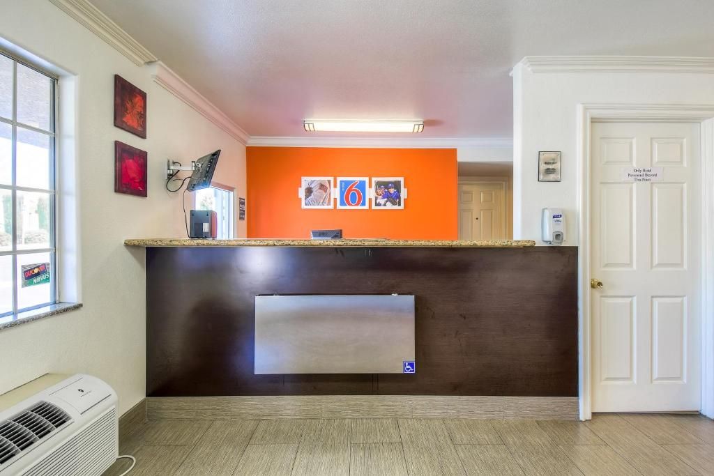 Un'area reception di un hotel con un bancone, un condizionatore d'aria a parete e una porta con un cartello.
