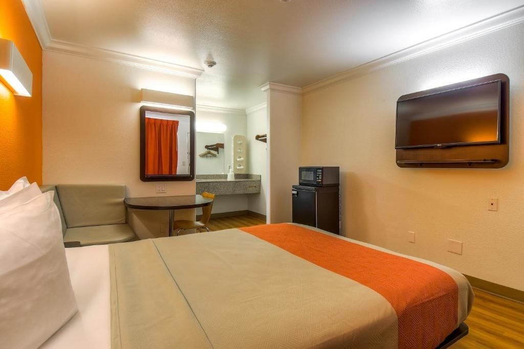 A hotel room with a bed, a small table, a chair, a TV, and a microwave.