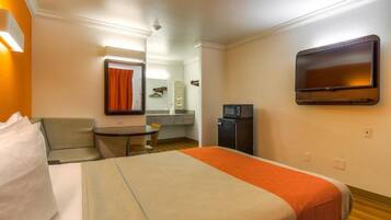 A hotel room with a bed, a small table, a chair, a TV, and a microwave.