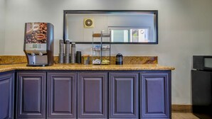 Una cocina con cafetera, tazas apiladas, microondas y armarios.